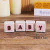 Five pink baby blocks with letters B A B Y arranged on a wooden surface.