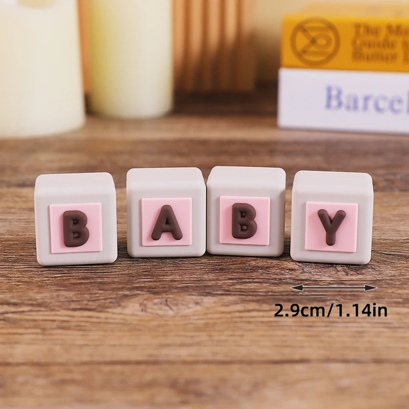Five pink baby blocks with letters B A B Y arranged on a wooden surface.