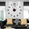 A modern wall clock with black numbers and hands is displayed above a black sofa.