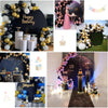 A dark gray and gold balloon photo backdrop decorated with flowers and elegant props for an event.