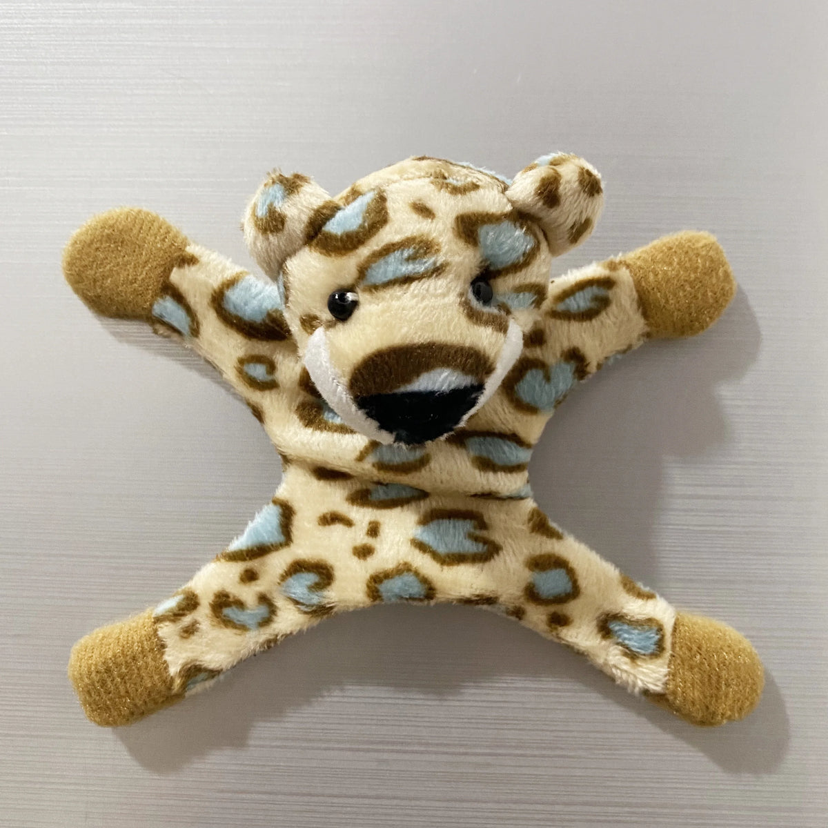 A plush toy resembling a leopard or cheetah, featuring light brown and blue spots, used as a fridge magnet.