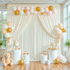 A soft pink and gold balloon floral backdrop with draped fabric for an elegant wedding or party setting.