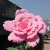 A large, vibrant pink artificial peony flower displayed against a dark background.