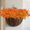 An artificial autumn bouquet of vibrant orange and yellow silk flowers displayed in a brown hanging planter on a white wall.