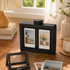 A black photo frame displaying a tropical landscape is shown on a wooden desk next to other decorative items.