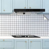 A kitchen featuring light blue cabinets, a black range hood, and a white subway tile backsplash.