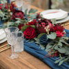 A floral arrangement featuring deep red and burgundy roses and eucalyptus leaves on a wooden table.