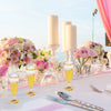 A display of elegant disposable plastic champagne flutes filled with yellow liquid on a white table.