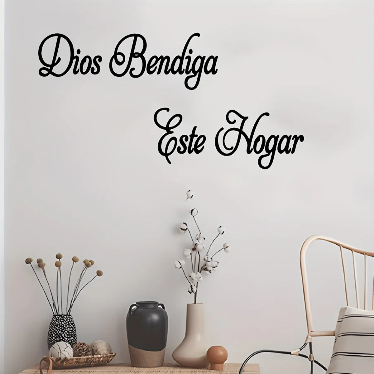 Schwarzer Schriftzug an einer weißen Wand, der 'Dios Bendiga Este Hogar' mit dekorativen Ästen und Keramik zeigt.