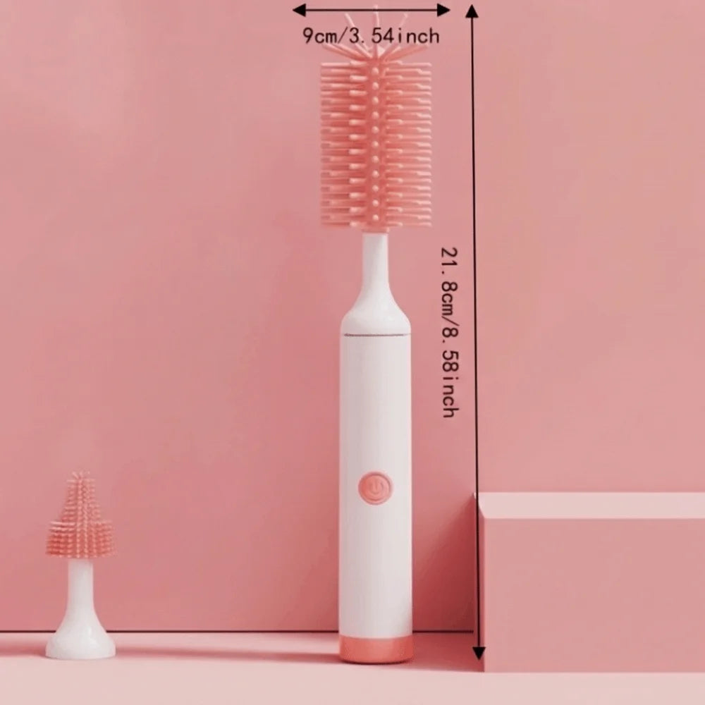 A pink electric baby bottle cleaning brush with a storage case is displayed against a pink wall.