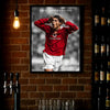 A framed poster of Cristiano Ronaldo celebrating, featuring a red shirt and white shorts against a dark background.