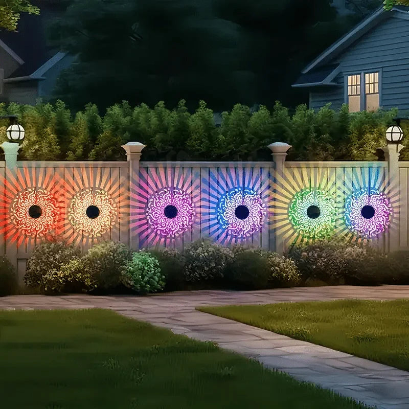 A row of illuminated mandala wall lanterns with various colors lining a wooden fence in a garden setting.