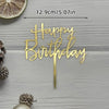 Gold acrylic birthday cake topper with happy birthday lettering on a wooden surface
