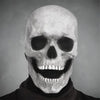 A grayscale close-up of a realistic human skull mask with a wide, toothy grin.