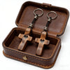 A handcrafted walnut cross keychain displayed inside a brown leather box.