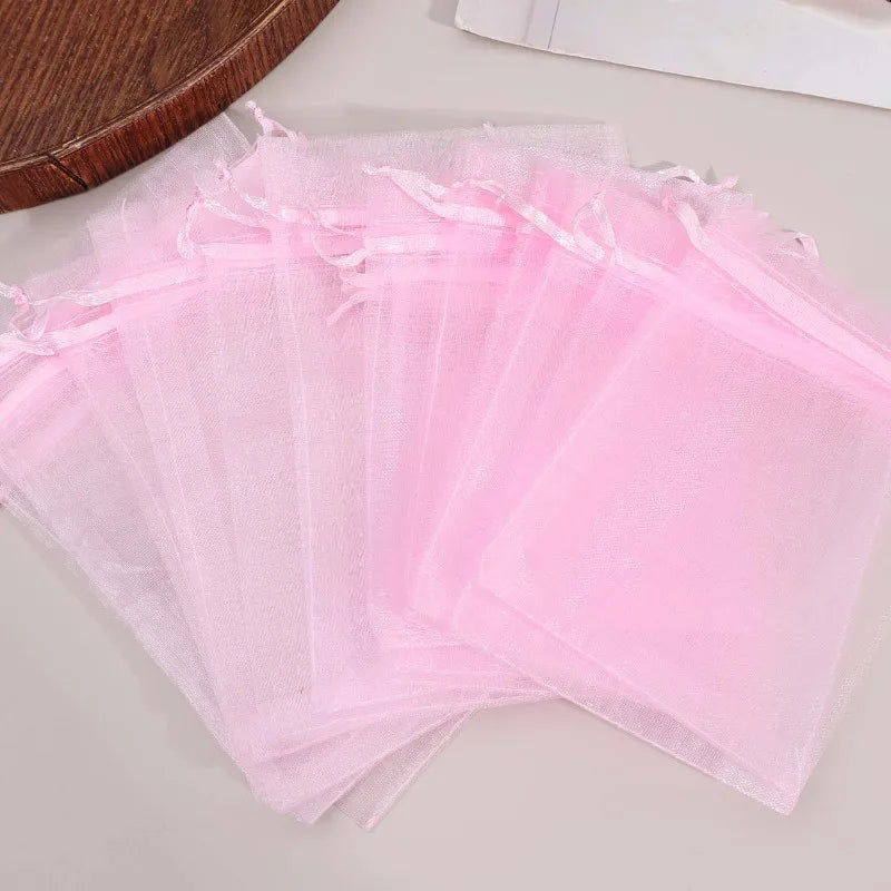 A stack of assorted pink organza drawstring gift bags laid out on a light surface.
