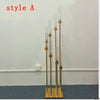 A tall gold metal candelabra set with eight glass candle holders displayed against a white wall.