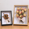 A wooden shadow box frame containing dried floral arrangements tied with sheer ribbon and natural greenery.