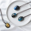 Three labradorite pendant necklaces with iridescent blue and gold flashes displayed on a white plate.