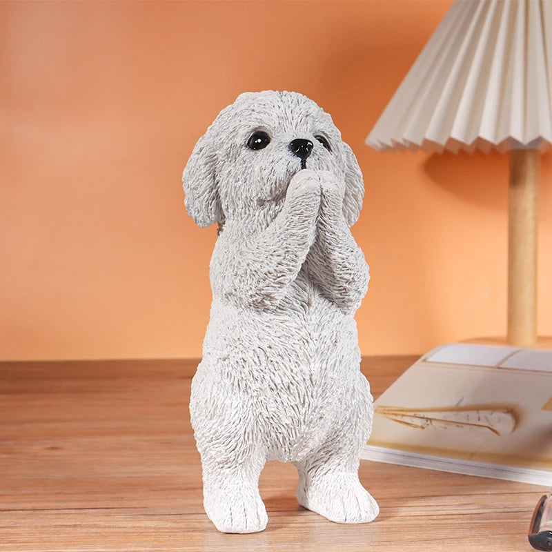 Une petite statue de chien en résine grise avec les pattes jointes, présentée sur une surface en bois.