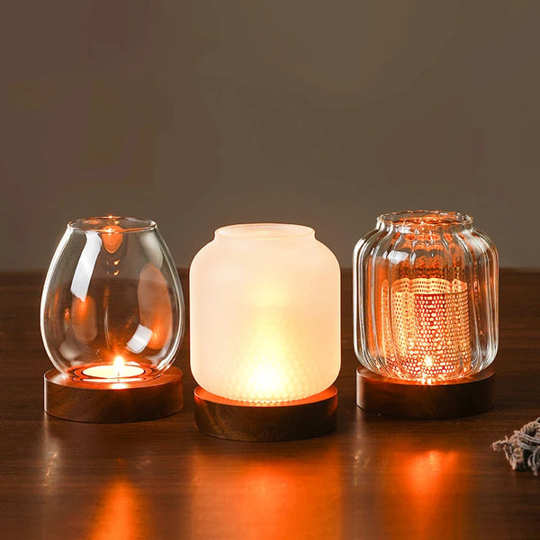 Three vintage wooden candle lanterns with glass covers glowing warmly on a dark wooden surface.