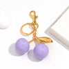 Gold-toned keychain featuring a purple resin cherry pendant on a white background.