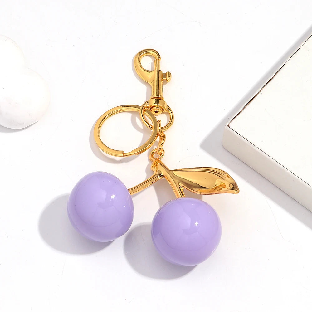 Gold-toned keychain featuring a purple resin cherry pendant on a white background.