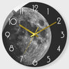 A black and white photograph of the moon face on a modern glass wall clock with gold hands.