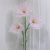 A large artificial silk pink poppy flower displayed on a green stand against a white background.