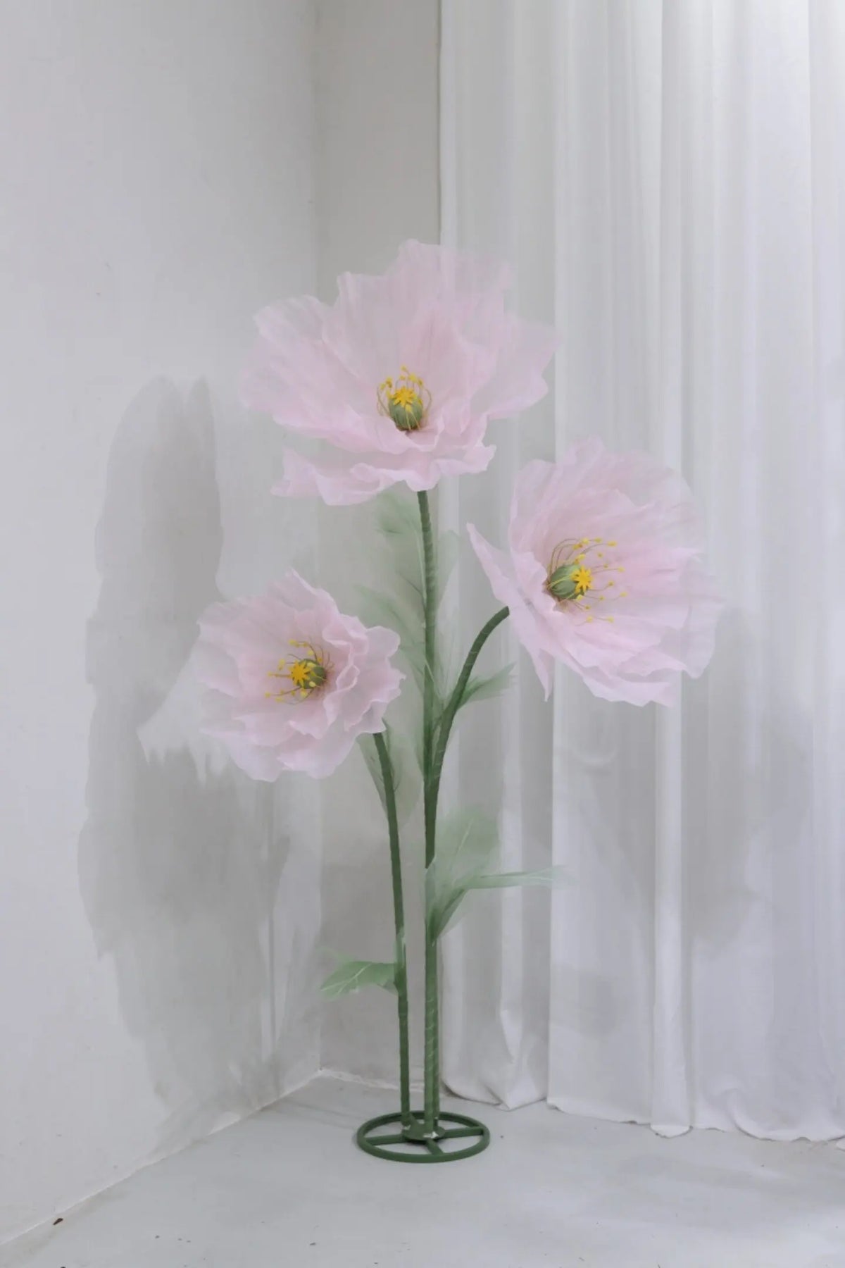 A large artificial silk pink poppy flower displayed on a green stand against a white background.