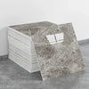 A stack of self-adhesive marble tile stickers is shown next to a single rectangular tile sample on a gray floor.