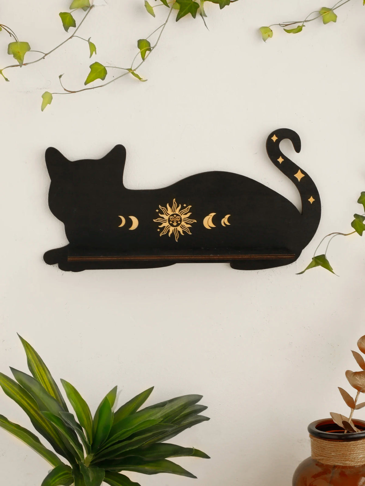 A black silhouette of a cat with gold moon phases and sun decoration on a white background.