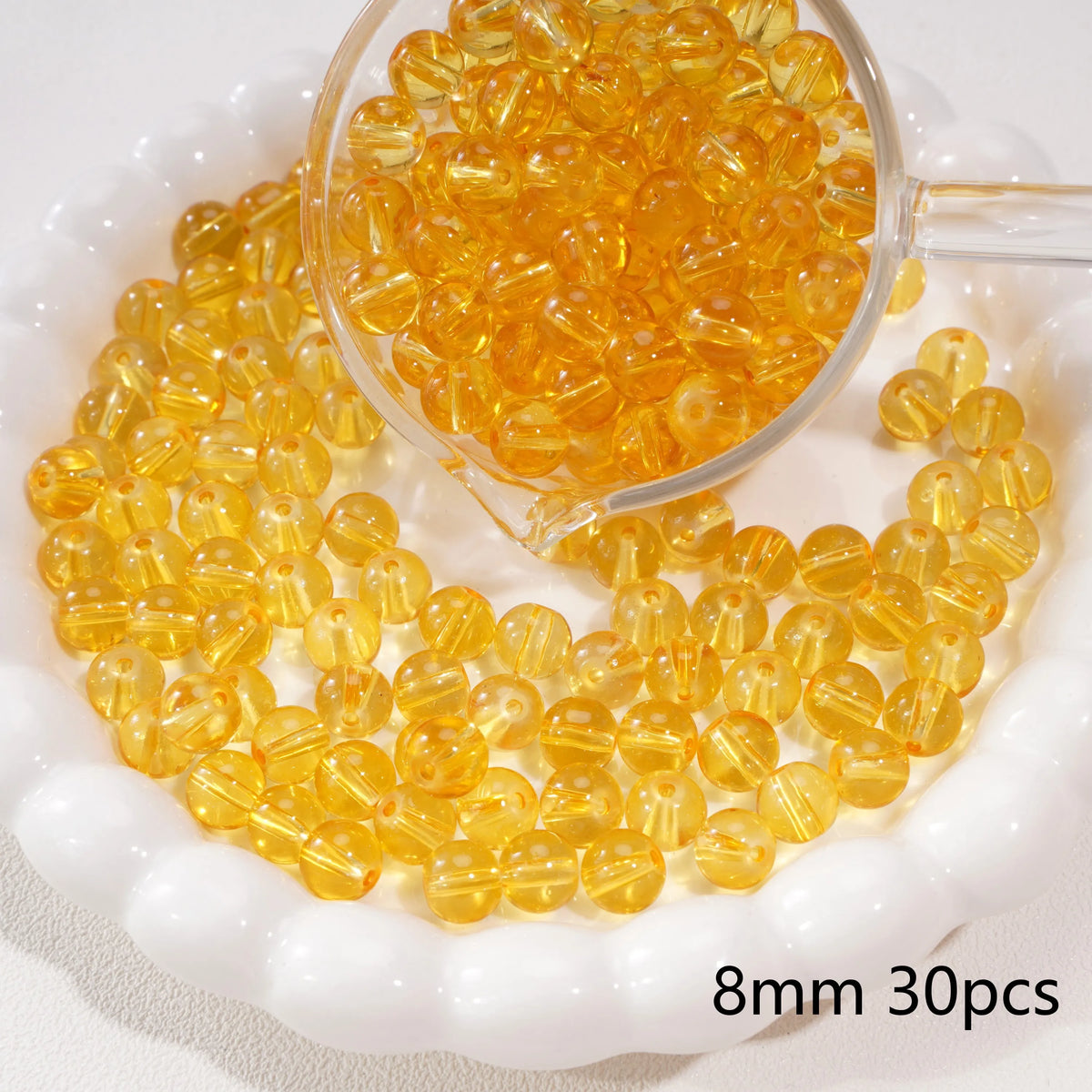 A clear glass dropper filled with round yellow spacer beads on a white dish.