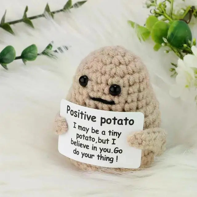 A handmade knitted plush doll resembling a potato with a handwritten sign that reads Positive potato