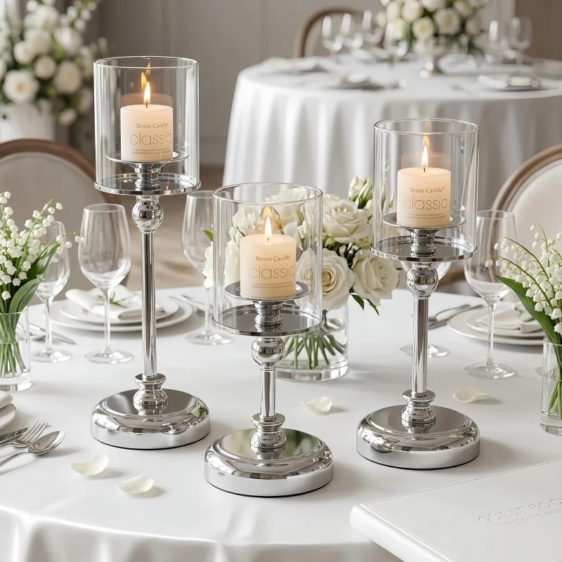 A silver metal pillar candle holder with a white candle is displayed on a white tablecloth for wedding or home decor.