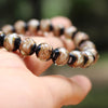 A hand holds a strand of handcrafted lampwork glass beads with gold accents, showing various shades of brown and black.