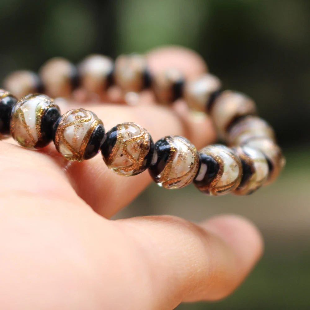 A hand holds a strand of handcrafted lampwork glass beads with gold accents, showing various shades of brown and black.