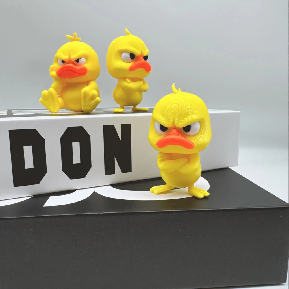 Three yellow 3D printed angry duck statues are displayed on a black box.