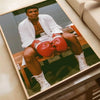 A portrait of a man in boxing attire sitting on a wooden bench, framed as wall art.