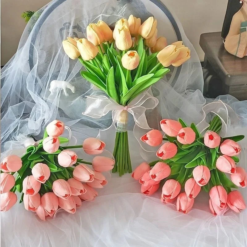 Un ramo de tulipanes artificiales rosas y amarillos dispuestos sobre tela blanca transparente.