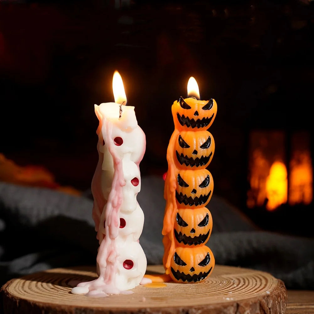 Two orange candles shaped like skulls and skeletons are lit in a dark, warm setting.