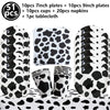 A set of cow print tableware including plates, cups, napkins, and a tablecloth for a farm-themed party.