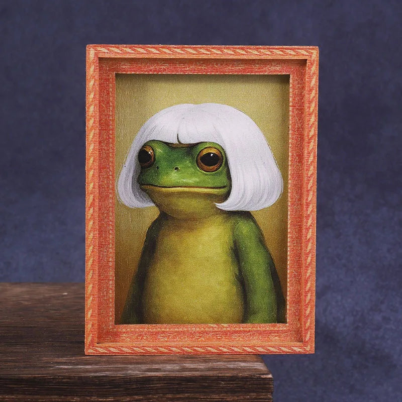 A framed illustration of a cute green frog with white hair, displayed in a wooden photo frame.