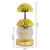 A decorative plant arrangement featuring pink and green flowers on a black stem, displayed in a clear glass pot on a gold bas