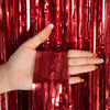 A hand holds a metallic red tinsel foil fringe curtain backdrop for parties.