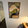 A framed canvas print depicting a landscape with rolling hills and a small figure, featuring earthy tones.