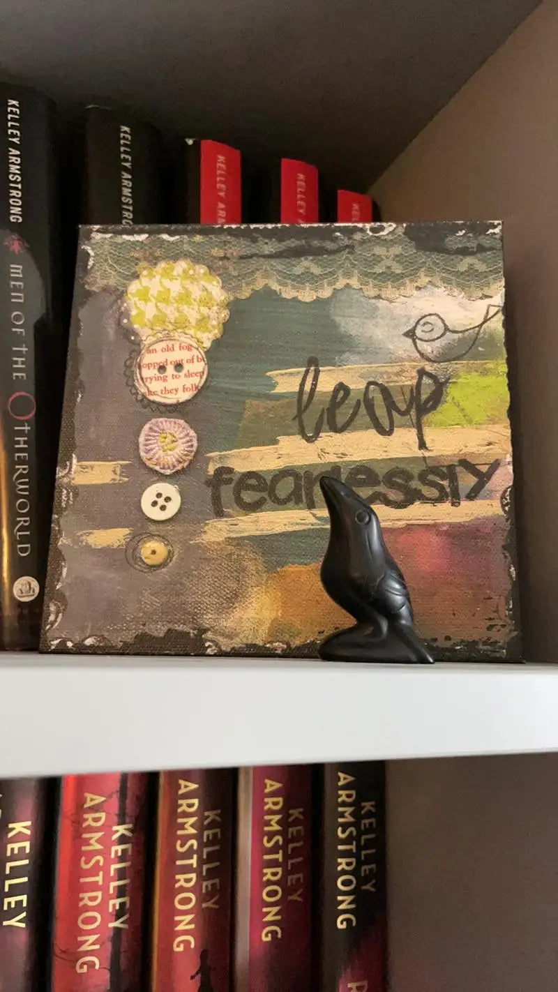 A black obsidian crow statue is displayed on a shelf among books.