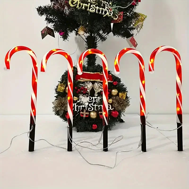 Five red and white candy cane pathway lights illuminate a decorated Christmas tree.