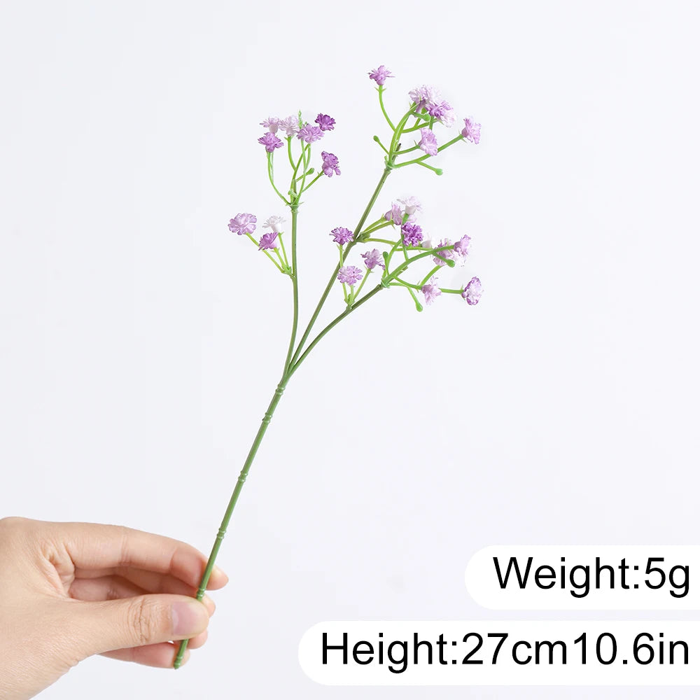 A slender stem of artificial baby's breath flowers with small purple clusters is held by a hand.