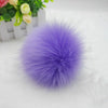 Pompon de cheveux en fausse fourrure violet posé sur une surface blanche à côté d'une plante en pot.
